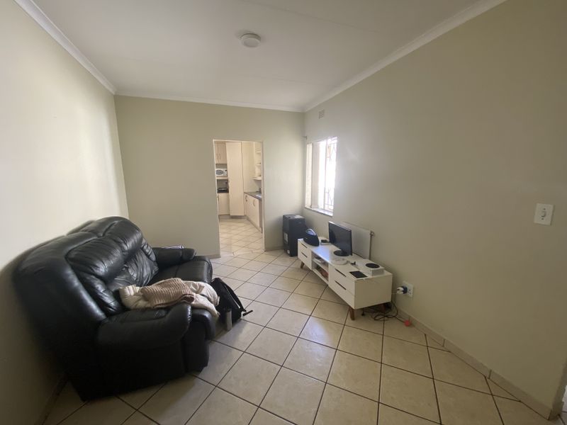 A living room featuring tiled flooring and a window with security bars, with an open doorway leading into the kitchen area.