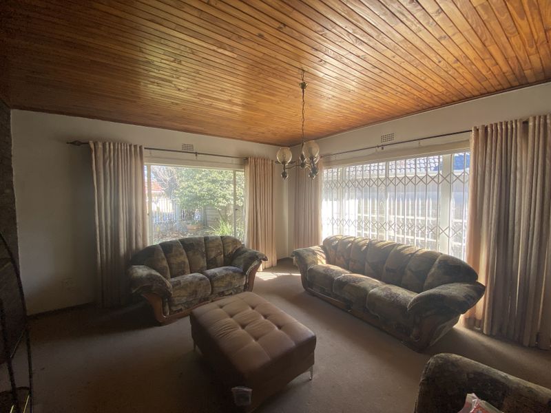 Spacious living room featuring a warm timber tongue and groove ceiling, large windows with security gates, and ample natural light.
