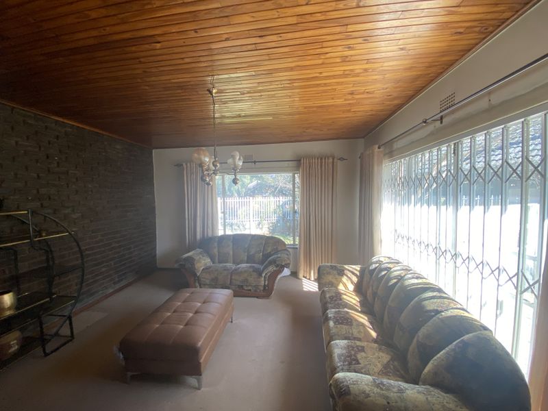 Spacious living room featuring a distinctive timber ceiling, an exposed brick feature wall, and large sliding doors with security gates leading to the exterior.