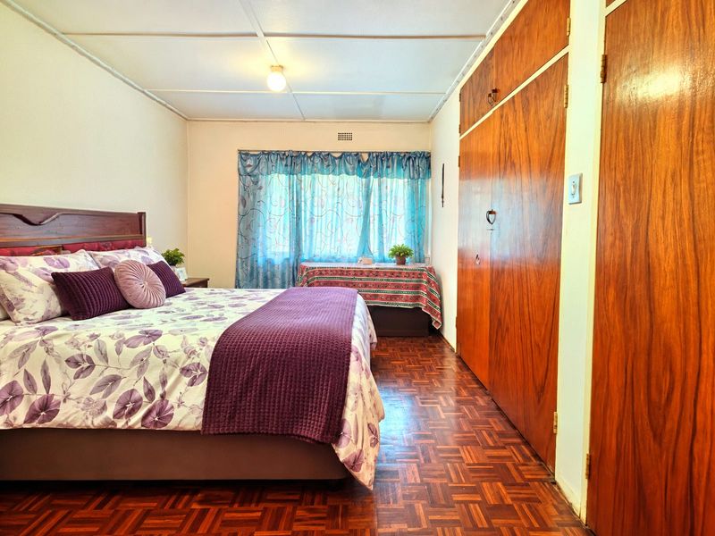 A bedroom featuring classic parquet flooring, built-in wooden cupboards, and a standard ceiling, offering a functional space with potential for modern updates.