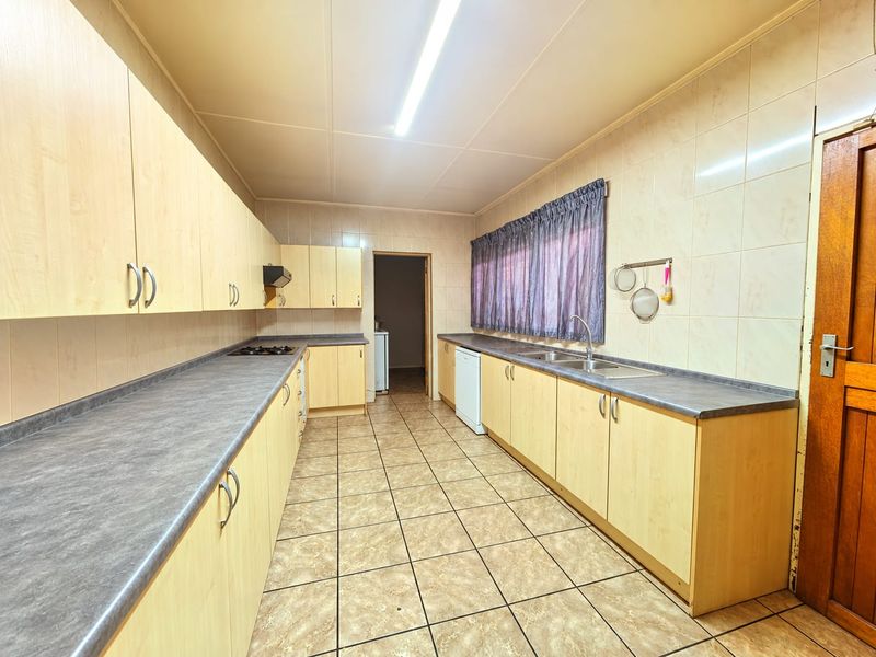 A functional kitchen featuring light wood-look cabinetry, dark laminate countertops, tiled walls, and floor, providing ample storage and workspace.