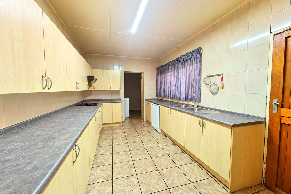 A functional kitchen featuring light wood-look cabinetry, dark laminate countertops, tiled walls, and floor, providing ample storage and workspace.