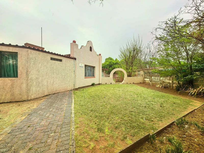 A rear exterior view of the property featuring a paved walkway, a grass lawn, and a decorative archway leading to the garden area.