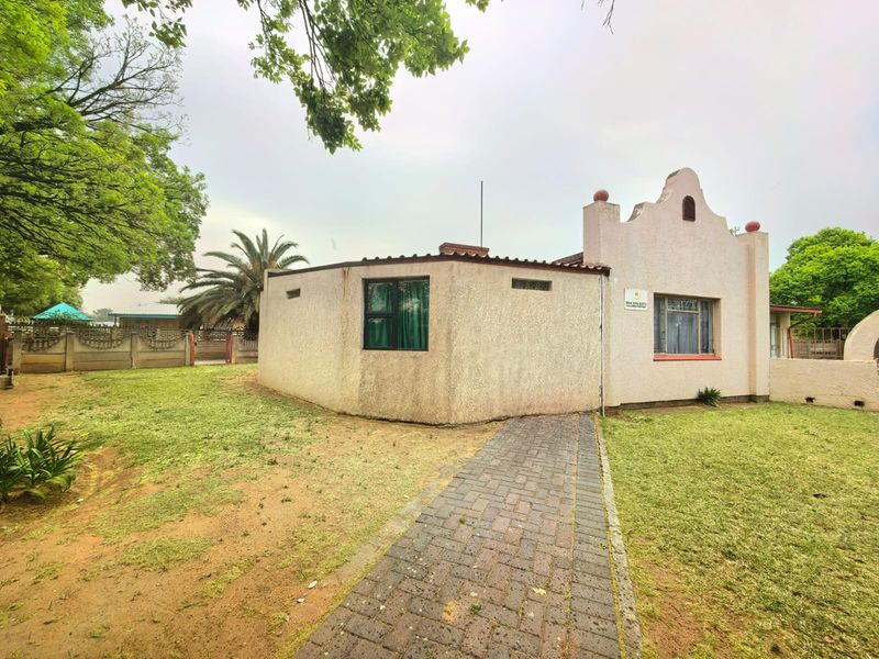 Rear view of the property featuring a paved walkway leading to the building, set within a garden area with boundary walling.