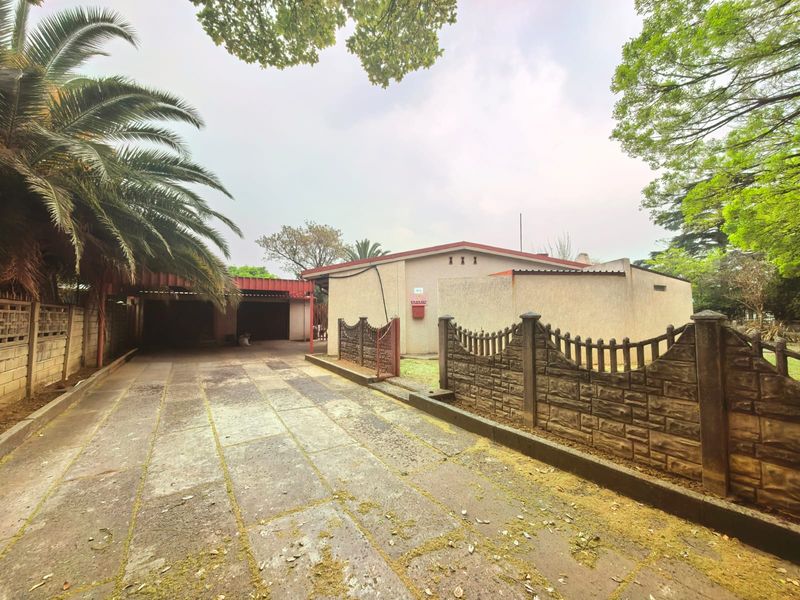 Front exterior view featuring a paved driveway, attached carport, and precast concrete boundary wall surrounding the property.