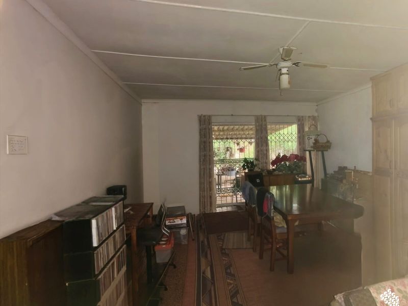 A living area featuring a ceiling fan, built-in cabinetry, and a sliding door leading to an outdoor space, requiring cosmetic updates to modernize the interior.