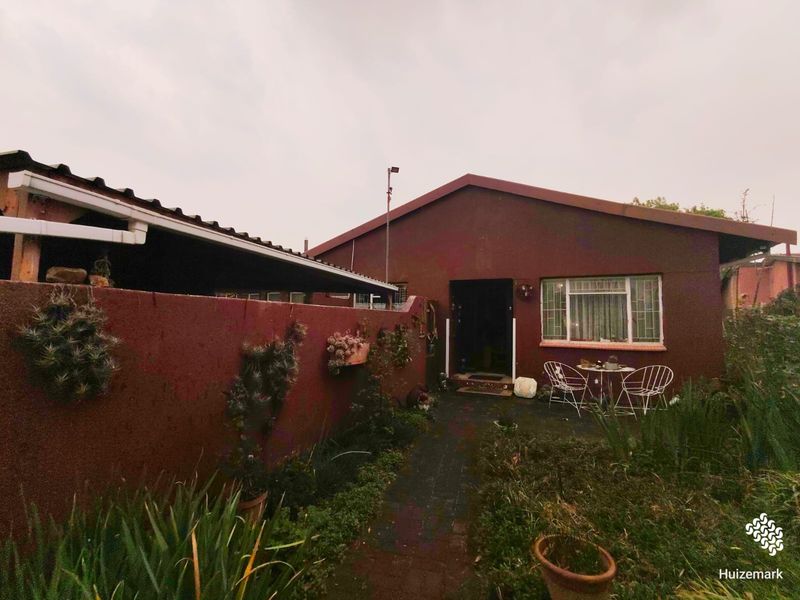 Rear view of the property featuring a covered patio area, paved walkway, and garden space with security bars on the windows.