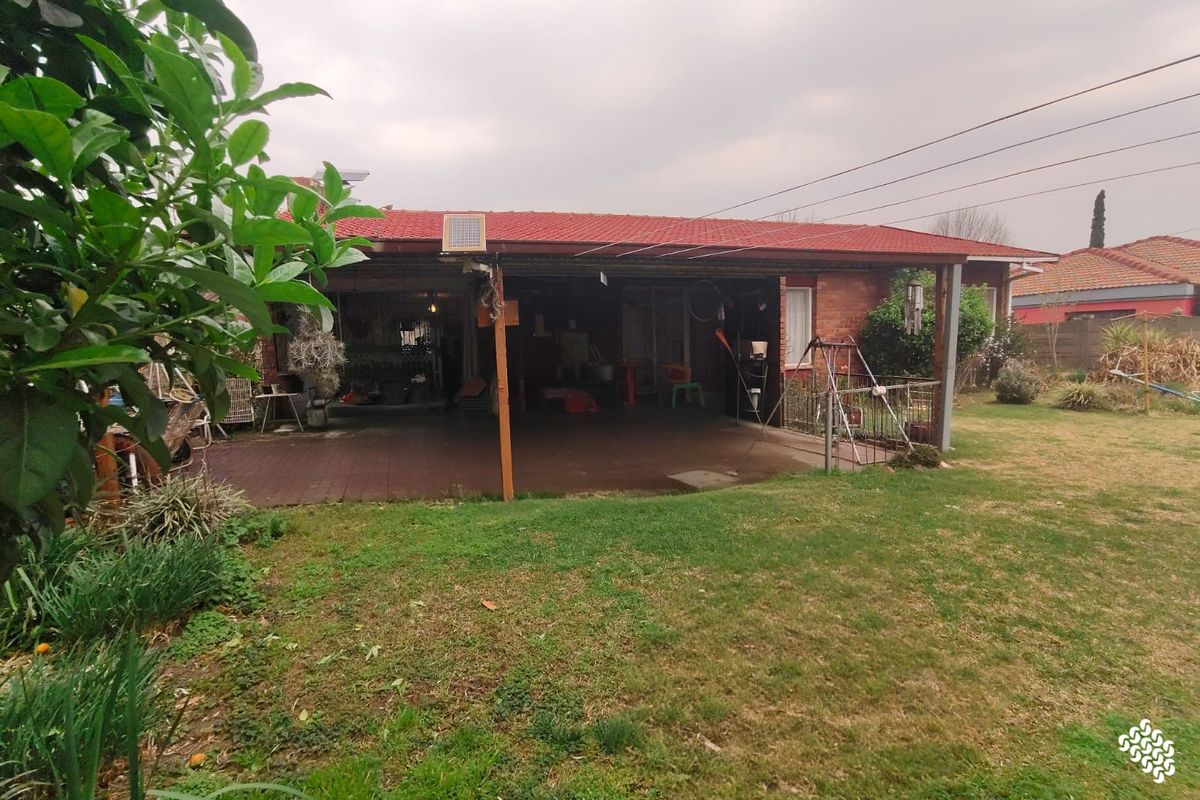 A rear view of the property featuring a covered patio area, brick exterior, and a spacious backyard lawn.
