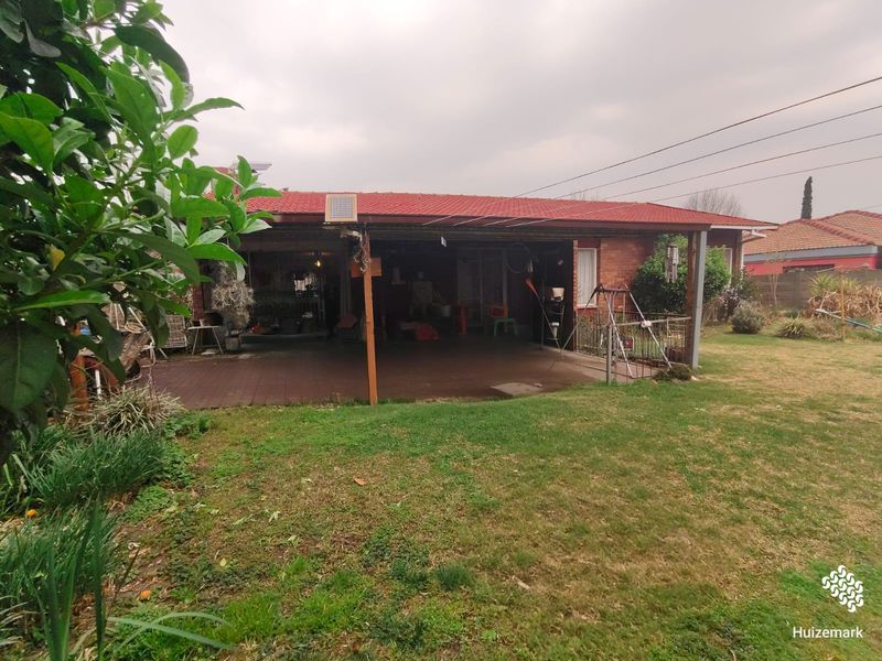 A rear view of the property featuring a covered patio area, brick exterior, and a spacious backyard lawn.