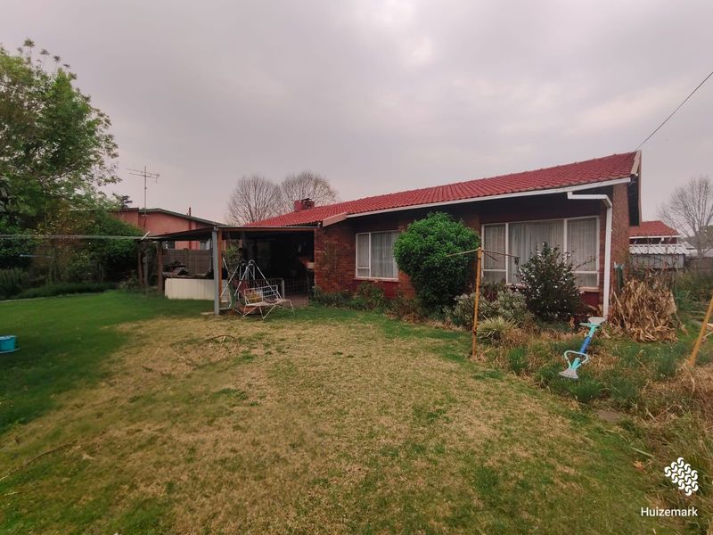 Rear view of a brick house featuring a red tiled roof and a covered patio area overlooking the garden.