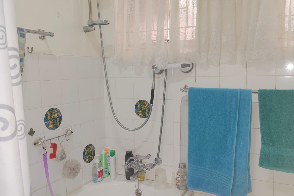 A functional bathroom featuring a built-in bathtub with a handheld shower attachment, tiled walls, and a window with security bars.