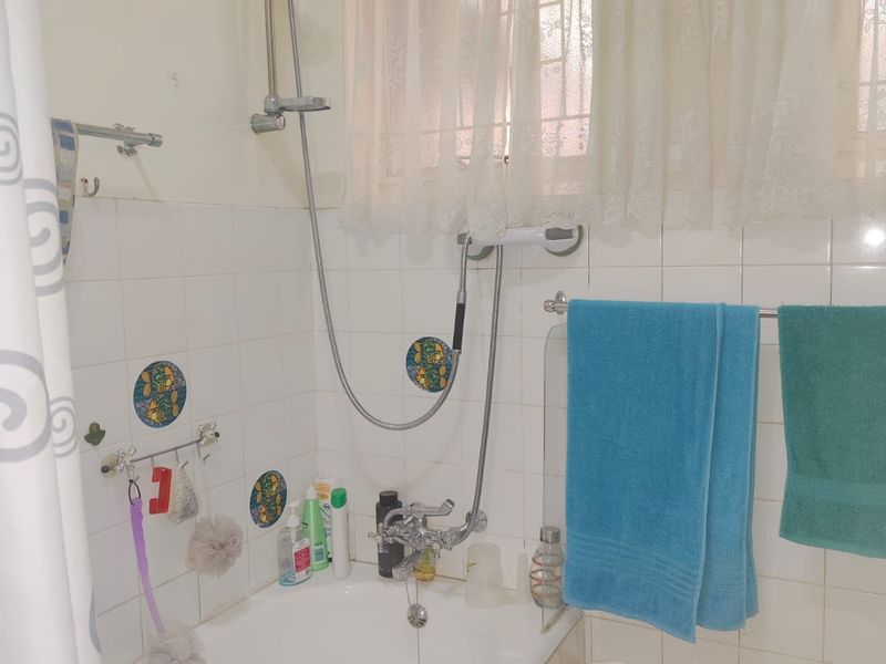 A functional bathroom featuring a built-in bathtub with a handheld shower attachment, tiled walls, and a window with security bars.
