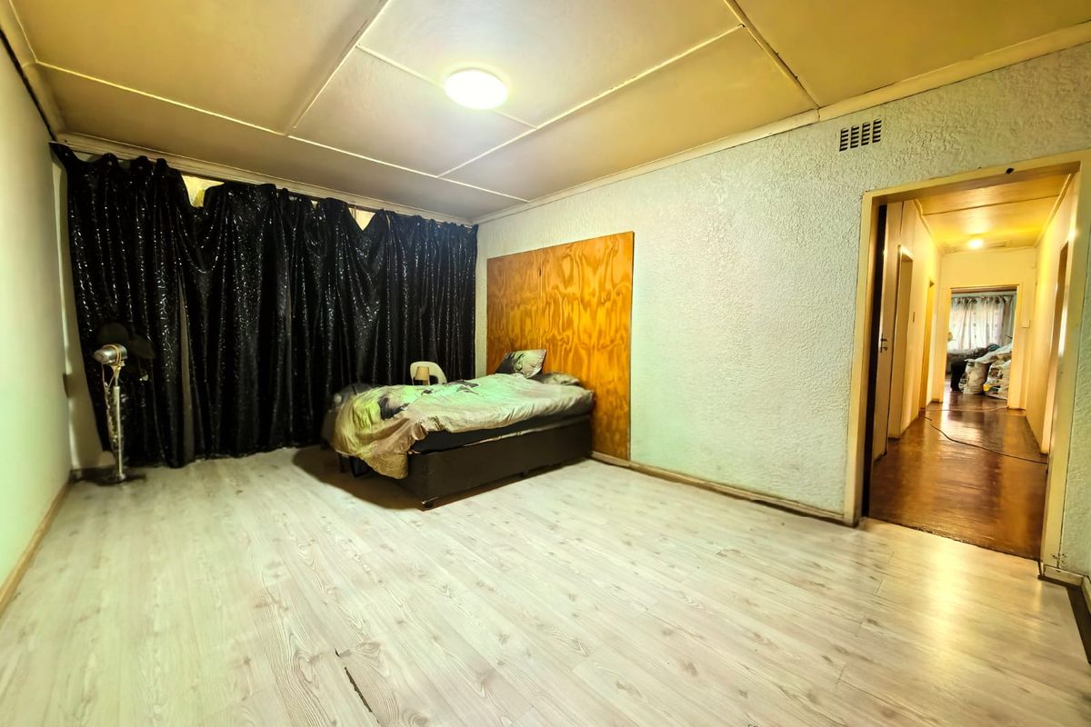 A bedroom featuring light-toned laminate flooring, a wooden headboard panel, and textured walls, leading into a hallway.