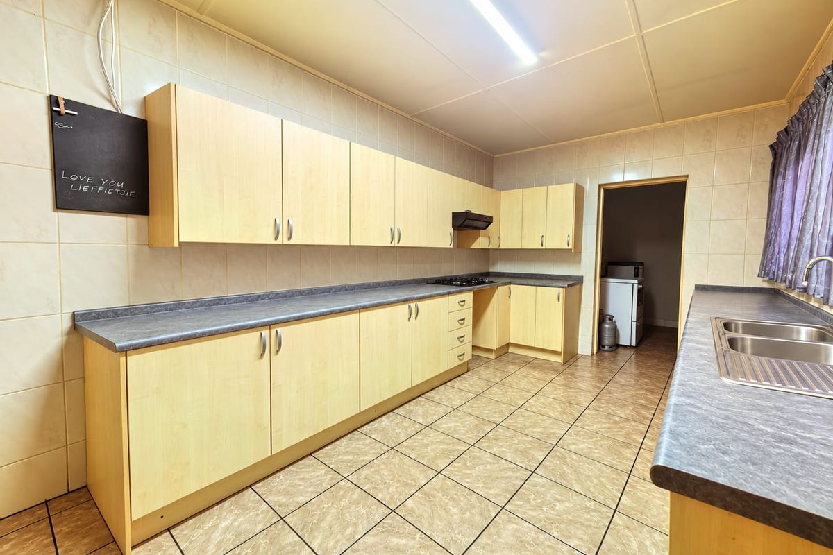 Functional kitchen featuring light wood-finish cabinetry, laminate countertops, a double stainless steel sink, built-in hob, and tiled flooring throughout.