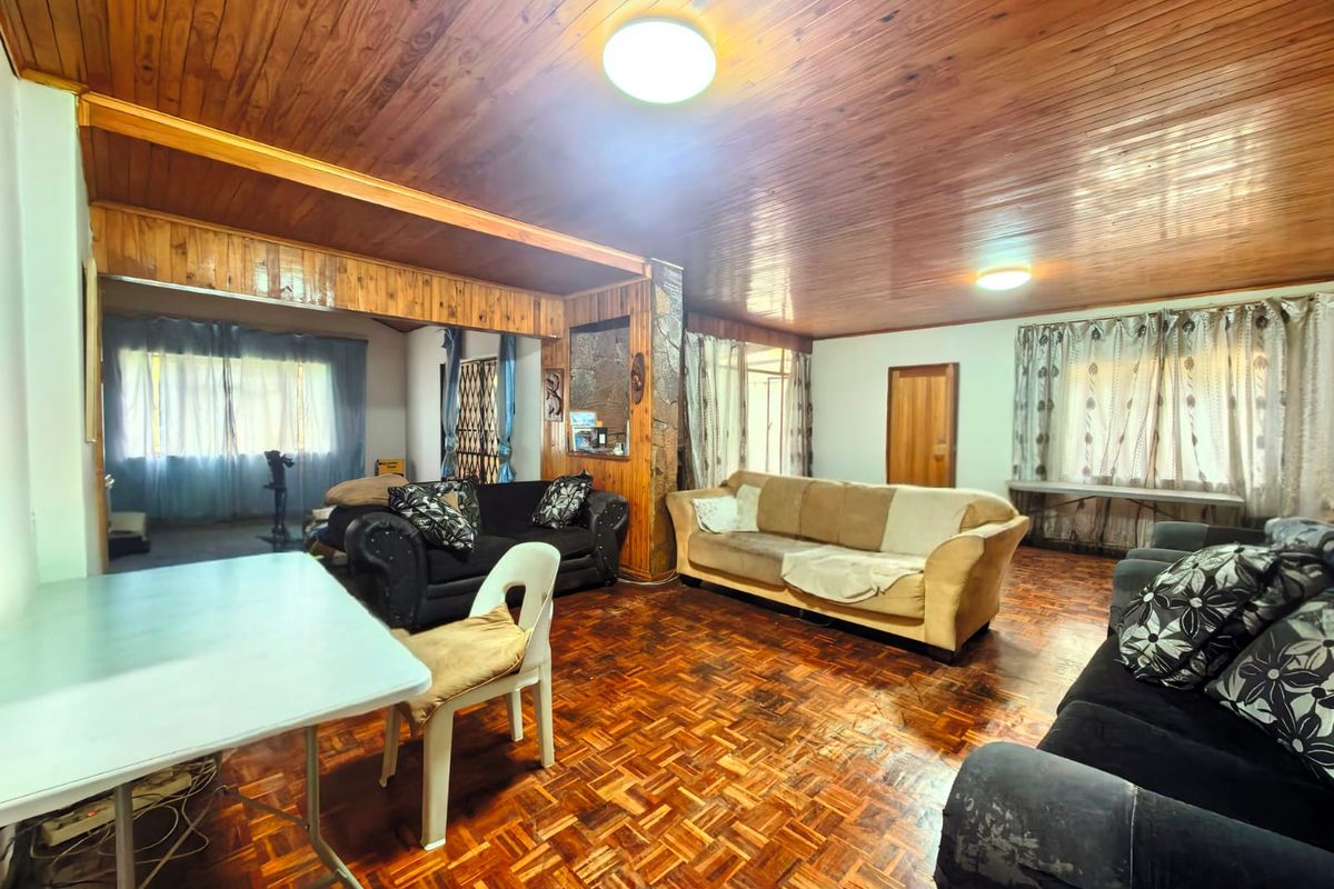 Spacious living area featuring traditional wooden parquet flooring and a warm timber-paneled ceiling with a stone accent wall.