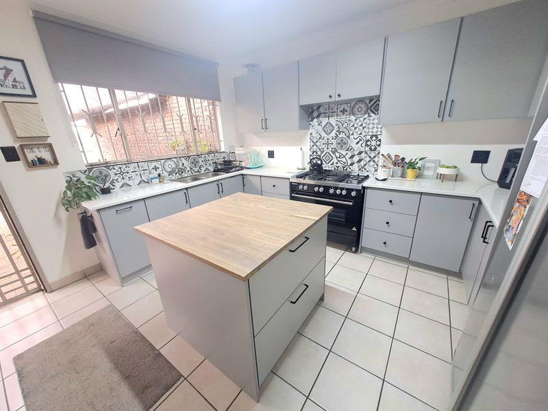 Modern kitchen featuring grey cabinetry, a central wooden-topped island, gas stove, and decorative patterned backsplash tiles.