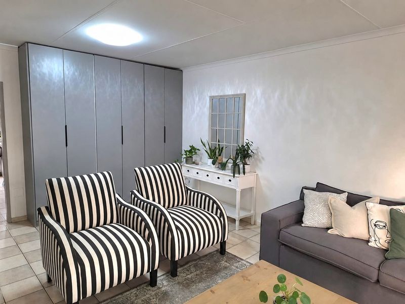 A well-maintained living room featuring neutral tiled flooring, a large wall of built-in grey cabinetry, and a bright, clean aesthetic.