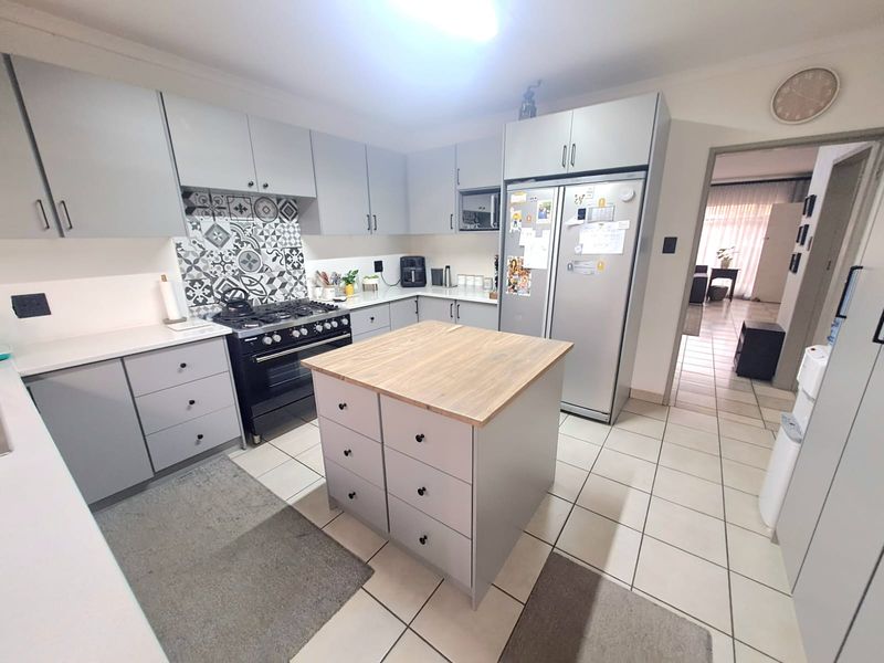 A well-maintained kitchen featuring grey cabinetry, a central island with a wooden countertop, a gas stove, and a decorative patterned tile backsplash.