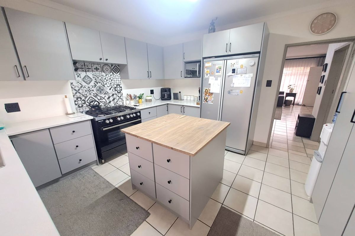 A well-maintained kitchen featuring grey cabinetry, a central island with a wooden countertop, a gas stove, and a decorative patterned tile backsplash.