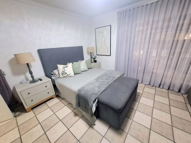 A well-lit bedroom featuring neutral tiled flooring and floor-to-ceiling sheer curtains, providing a clean and functional living space.