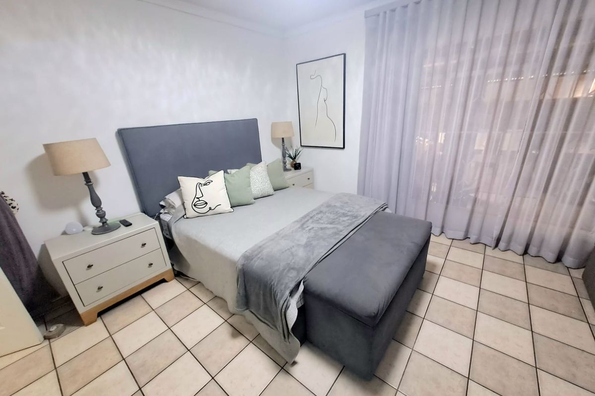 A well-lit bedroom featuring neutral tiled flooring and floor-to-ceiling sheer curtains, providing a clean and functional living space.