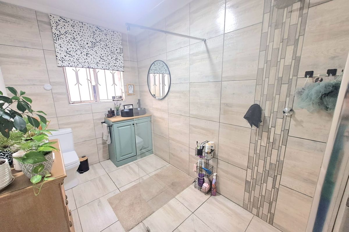 Modern bathroom featuring floor-to-ceiling neutral tiling, a walk-in shower with glass screen, a vanity cabinet with basin, and a toilet.