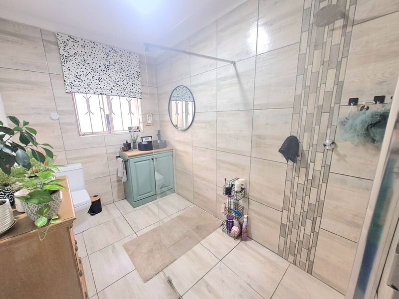 Modern bathroom featuring floor-to-ceiling neutral tiling, a walk-in shower with glass screen, a vanity cabinet with basin, and a toilet.