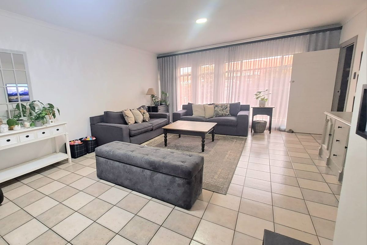 Spacious living room featuring neutral tiled flooring, recessed lighting, and large windows with sheer curtains, providing a bright and open atmosphere.
