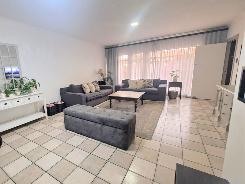 Spacious living room featuring neutral tiled flooring, recessed lighting, and large windows with sheer curtains, providing a bright and open atmosphere.