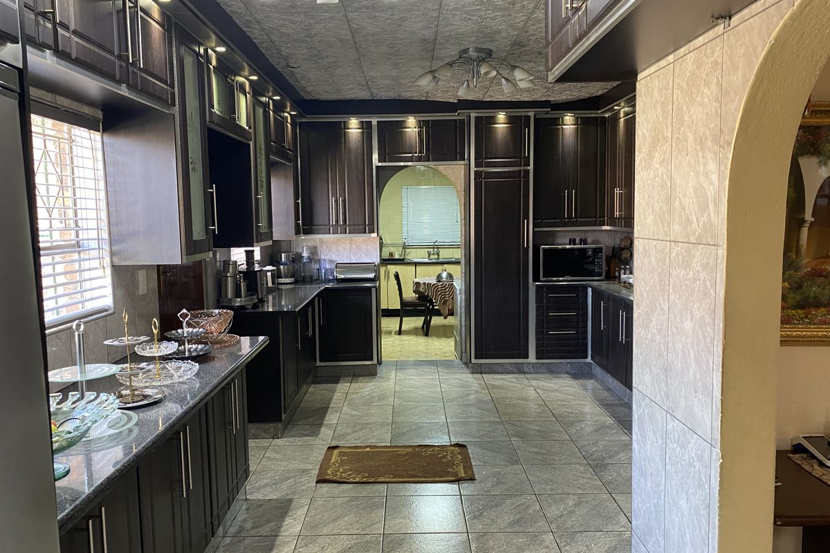 A well-maintained kitchen featuring dark wood cabinetry, granite countertops, tiled flooring, and an archway leading to an adjacent dining area.
