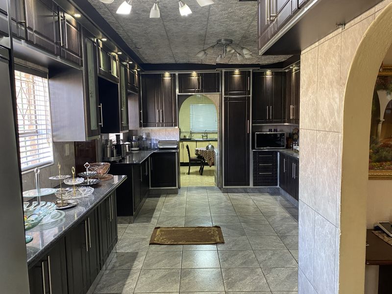 A well-maintained kitchen featuring dark wood cabinetry, granite countertops, tiled flooring, and an archway leading to an adjacent dining area.