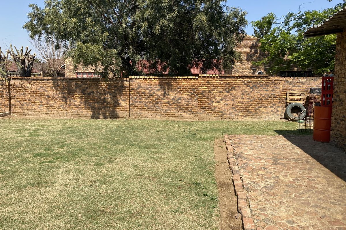 A private rear garden featuring a well-maintained lawn, a brick-paved patio area, and a solid brick boundary wall providing privacy.