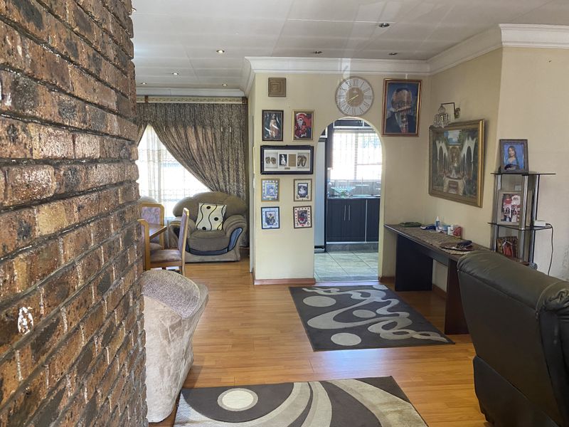 Open plan living area featuring laminate flooring, an exposed brick feature wall, and an arched entryway leading to the kitchen.