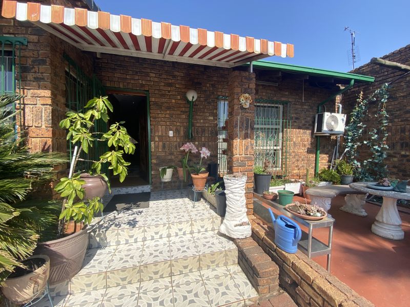 A covered brick patio area featuring tiled steps, a retractable striped awning, and security bars on the windows.
