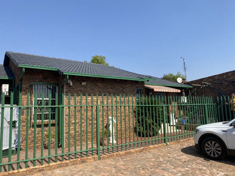 Front view of a face brick house featuring a tiled roof, security fencing, and a paved driveway area.