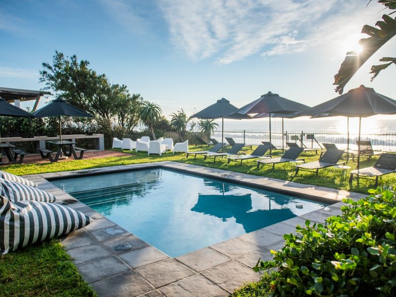 A well-maintained outdoor swimming pool area featuring stone coping, set against a scenic coastal backdrop with established garden surroundings.