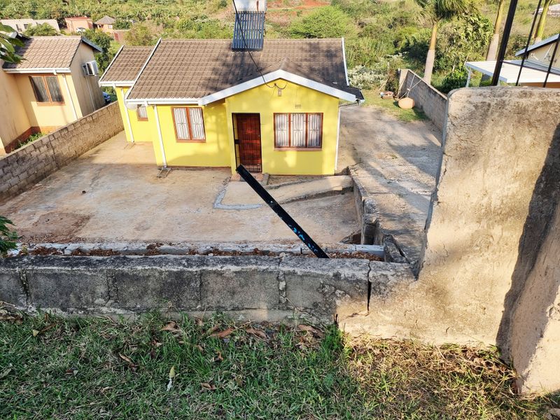 A detached single-story house featuring a tiled roof, solar water heater, and a concrete driveway, set within a walled perimeter property.