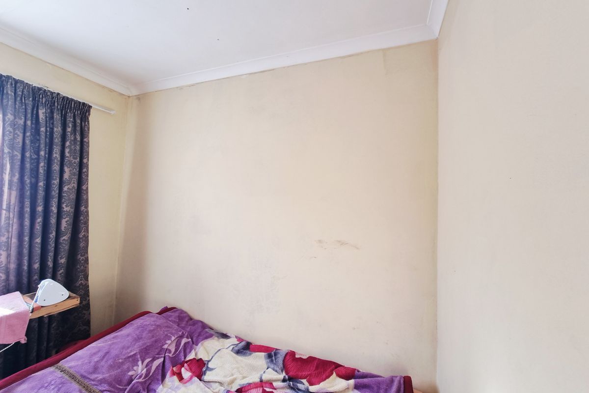 A bedroom corner featuring plain walls with visible scuff marks and a standard ceiling cornice.