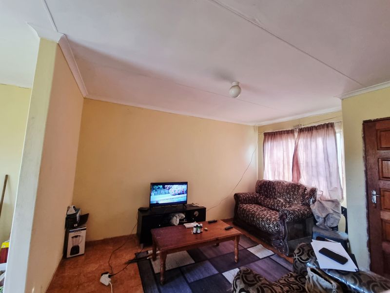 A living room featuring tiled flooring, cove cornicing, and a timber door, currently showing signs of wear on the walls and ceiling.