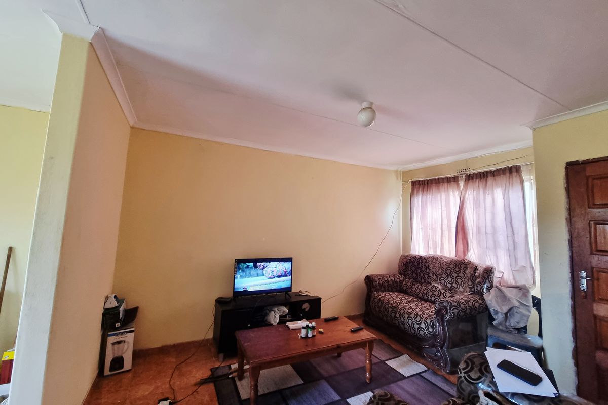 A living room featuring tiled flooring, cove cornicing, and a timber door, currently showing signs of wear on the walls and ceiling.