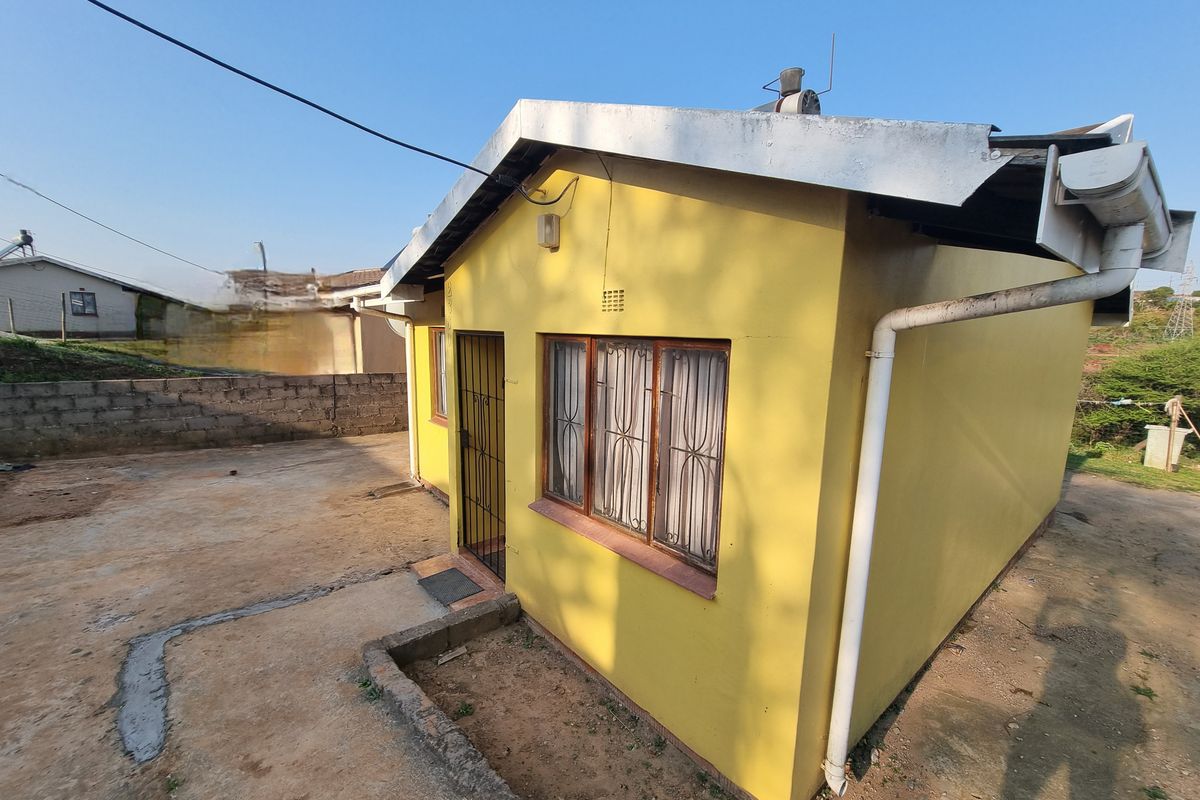Rear exterior view of a yellow painted house featuring metal window frames, security gate, and basic concrete apron area.
