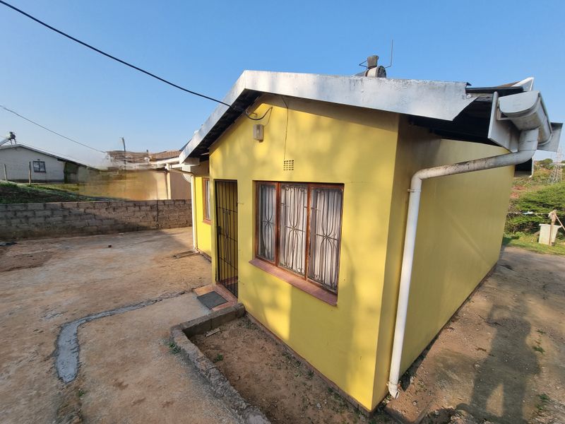 Rear exterior view of a yellow painted house featuring metal window frames, security gate, and basic concrete apron area.