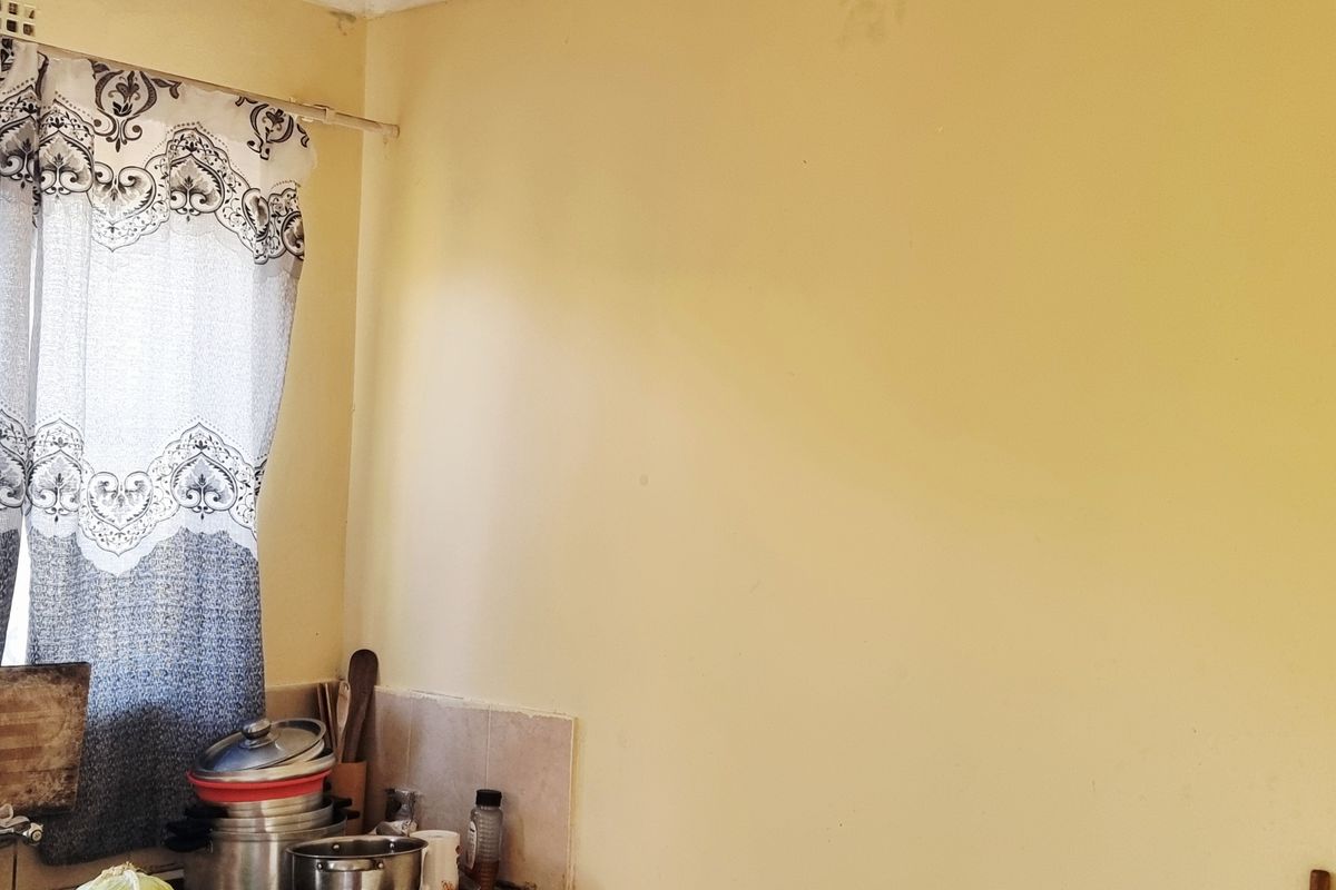 A kitchen corner featuring a stainless steel sink, stone countertop, and tiled splashback, requiring cosmetic updates to the wall finishes.