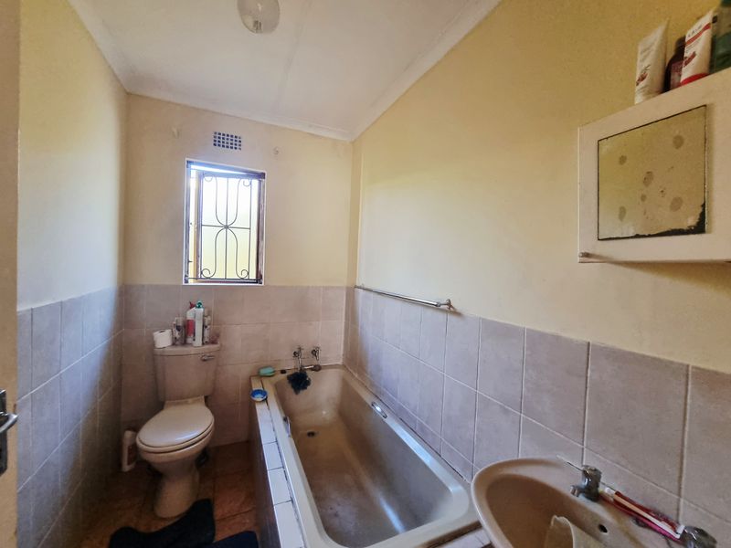 A dated bathroom featuring a standard bathtub, pedestal basin, and toilet, requiring cosmetic updates and modernization of fixtures and finishes.