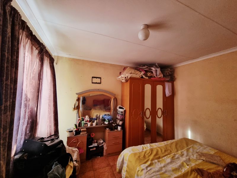 A bedroom featuring tiled flooring and standard ceiling lighting, currently showing signs of wear on the wall surfaces.