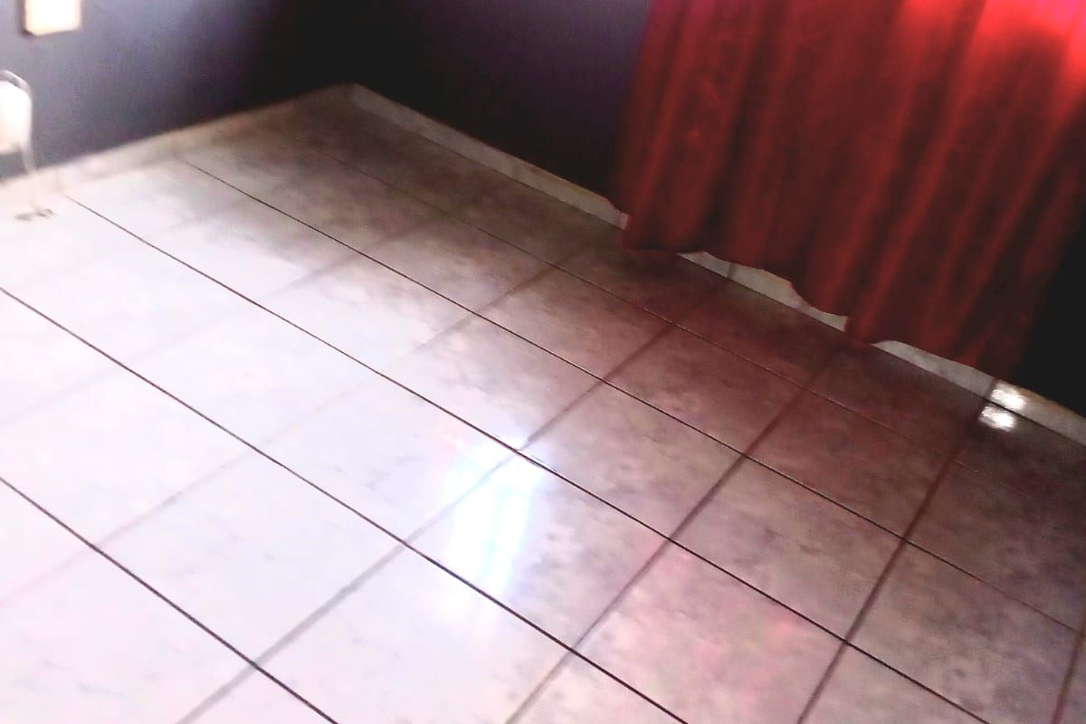 An empty bedroom featuring tiled flooring and a window with security bars, awaiting personal touches or staging.