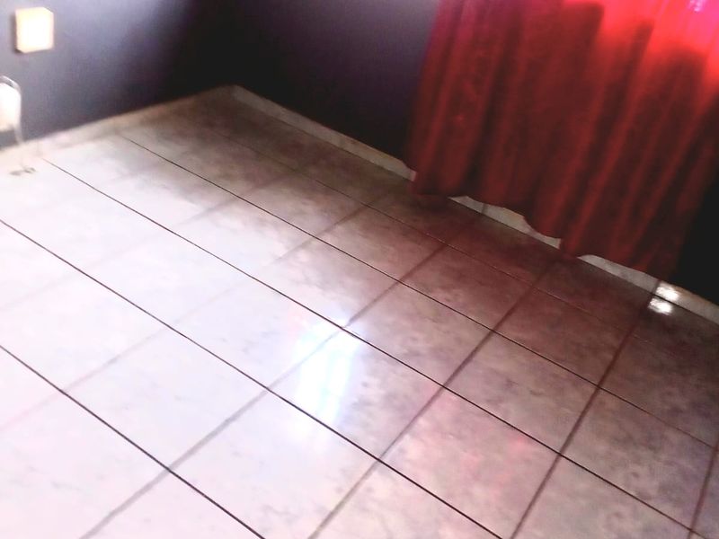 An empty bedroom featuring tiled flooring and a window with security bars, awaiting personal touches or staging.