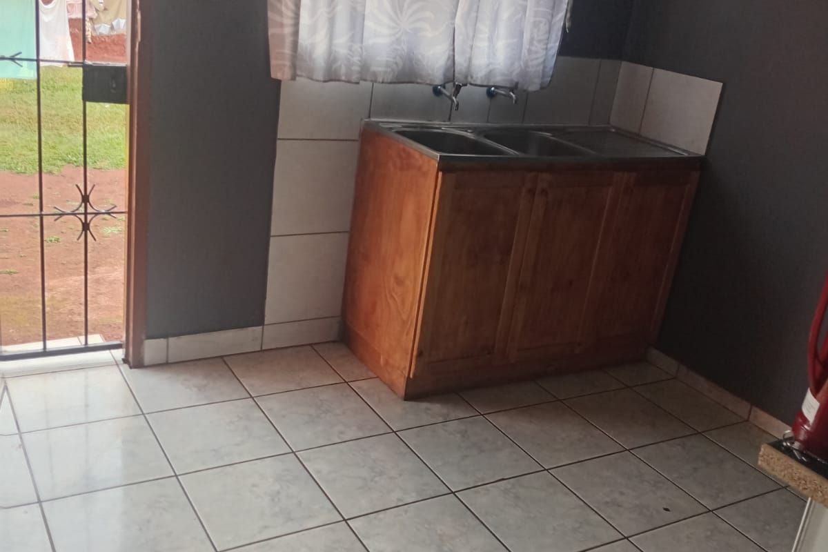 A functional laundry area featuring a double sink with a wooden vanity cabinet, tiled flooring, and direct access to the rear garden.