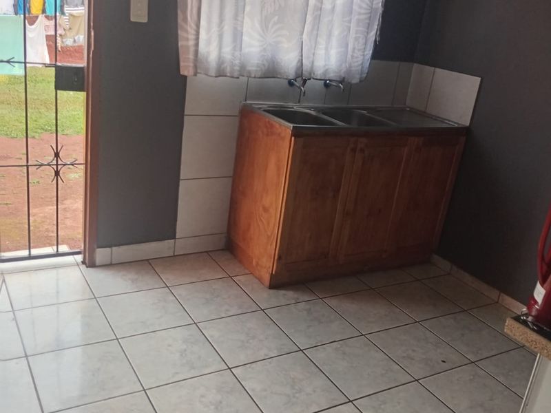 A functional laundry area featuring a double sink with a wooden vanity cabinet, tiled flooring, and direct access to the rear garden.