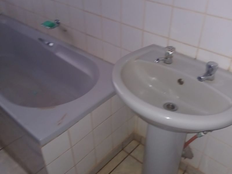 A dated bathroom featuring a pedestal basin and a bathtub with tiled walls and flooring, requiring cosmetic updates and maintenance.